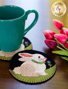 two coasters on a table with pink tulips and a green coffee cup