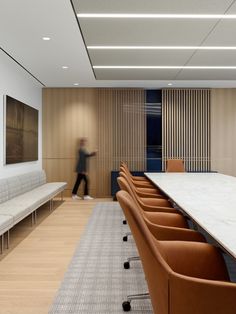 a man walking past a long table in a conference room with leather chairs and benches