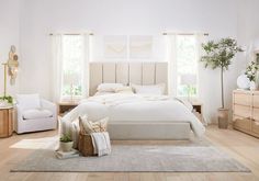 a bedroom with white walls and wooden floors, large bed in the center surrounded by beige furniture