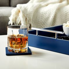 a glass of whiskey sitting on top of a table next to a tray with food