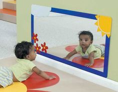 two toddlers playing in front of a mirror with their feet on the ground and looking at each other