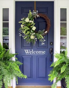 a blue front door with two plants and a welcome sign on the front porch area