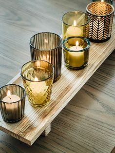 three candles sitting on top of a wooden table next to other glass vases and candle holders