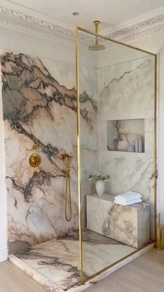 a bathroom with marble walls and flooring, gold trimming on the shower door