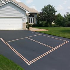 an empty basketball court in front of a house with grass and bushes around it,