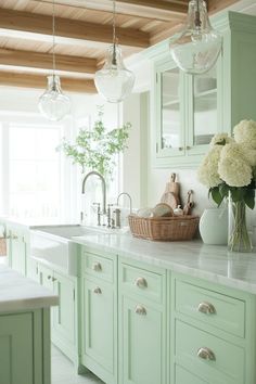 a kitchen with green cabinets and marble counter tops, white flowers in a vase on the island