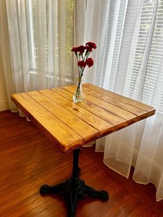 a vase with flowers on top of a wooden table in front of a curtained window