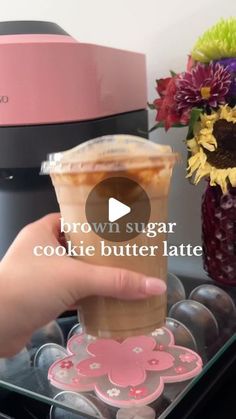 someone is holding up a drink in front of a coffee maker with flowers on it