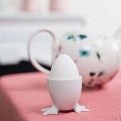 an egg sitting on top of a table next to a white teapot and cup