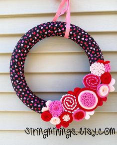 a decorated wreath hanging on the side of a house with pink and red felt flowers