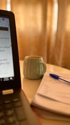 an open laptop computer sitting on top of a table next to a cup and pen