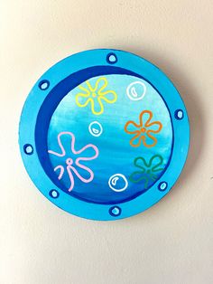 a blue circular wall hanging with flowers painted on the side and circles at the bottom