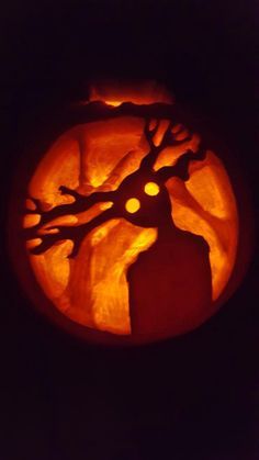 a carved pumpkin with an image of a tree on it's face in the dark