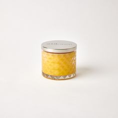 a yellow candle is sitting on a white surface and it has a silver lid that says,