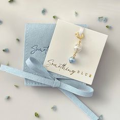 a card with a blue ribbon tied around it and a pearl bead on the end