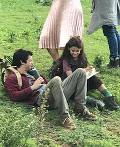 two people sitting on the ground with one holding a book and talking to another person