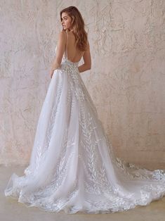 a woman in a white wedding dress standing against a wall with her back to the camera