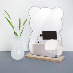 a white desk with a laptop on it next to a large mirror and plant in a vase