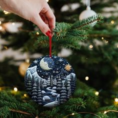 a hand holding an ornament on top of a christmas tree