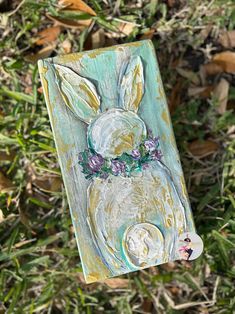 a painting of a white rabbit with purple flowers on it's head sitting in the grass