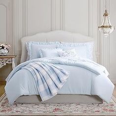 a white bed with blue comforter and pillows in a room next to a chandelier