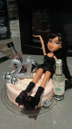 a doll sitting on top of a cake next to a bottle of boojute