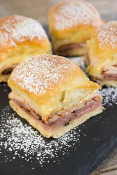 four pastries sitting on top of a black plate covered in powdered sugar next to each other