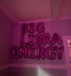 the words big library energy are lit up in bright pink neon letters on a wall