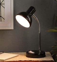 a desk lamp sitting on top of a wooden table next to a notebook and plant