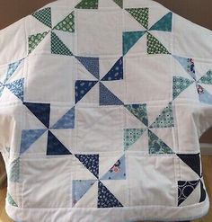 the back of a quilted jacket with blue and green triangles on it, sitting on top of a wooden table