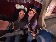 two girls wearing mickey mouse ears and sunglasses on a train car with their reflection in the mirror