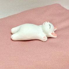 a white cat figurine laying on top of a pink bed sheet with its eyes closed