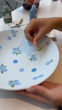 a person holding a white plate with blue flowers on it and another hand reaching for something in the bowl