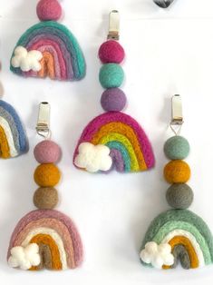 several felted objects are arranged on a white surface, including rainbows and clouds