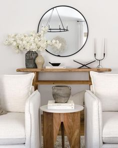 a living room with two chairs and a table in front of a round mirror on the wall