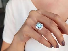 a woman's hand wearing a ring with an aqua blue topazte surrounded by diamonds