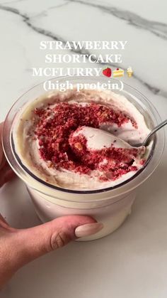 a person holding a spoon in a bowl filled with ice cream and raspberry shortcake