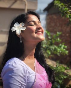 a woman with long black hair wearing a white flower in her hair and looking up at the sky