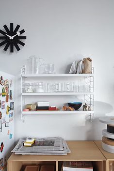 there is a clock on the wall next to some shelves with magazines and other items