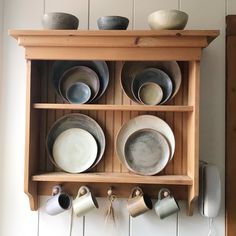 a wooden shelf with bowls and cups on it's sides, hanging from the wall