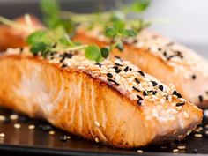 two salmons with sesame seeds and garnishes on a black platter