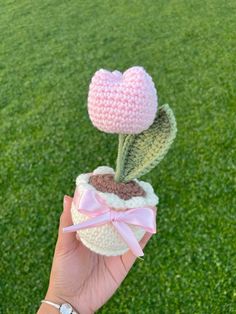 a hand holding a crocheted flower with a pink bow on it's end