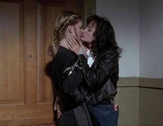 two women kissing each other in front of a wooden door