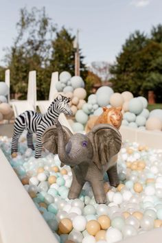 an elephant and zebra statue in a bubble filled pool surrounded by fake rocks, balls, and trees