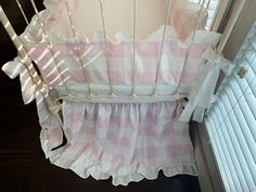 a baby crib with pink and white checkered bedding on it's side