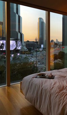 a bed sitting next to a large window in a bedroom under a sky line with tall buildings