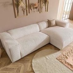 a white couch sitting on top of a hard wood floor next to a wall with pictures above it