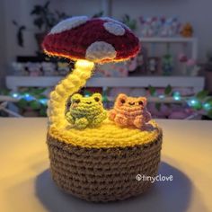 a crocheted basket with two small owls sitting under a mushroom light on top of it