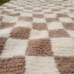 a brown and white checkered blanket laying on the ground with grass in the background