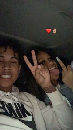 two people sitting in a car making peace signs